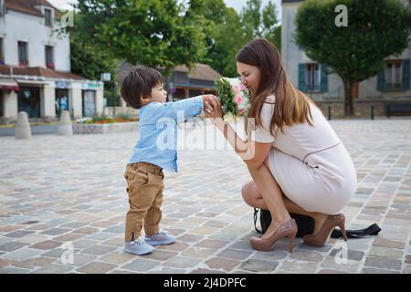 Ragazzo misto di razza congratulandosi con la madre e dando il suo bouquet di fiori Foto Stock