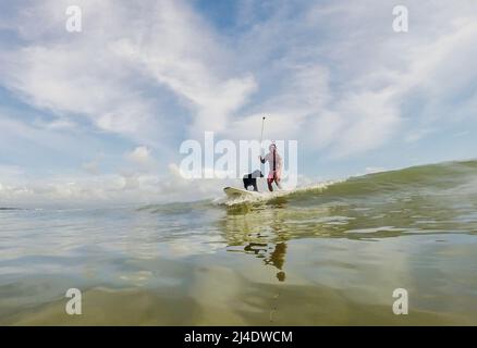 Provincia di Aurora, Filippine. 14th Apr 2022. Il surfista Mario Cardama Jr. E il cane Gordy surf in una spiaggia nella provincia di Aurora, nelle Filippine, 14 aprile 2022. Fondato nel 2016, il Dog Collective è costituito da appassionati di surf che sono anche amanti del cane. Trascorrono il loro tempo libero insegnando ai loro animali domestici adottisi a fare un giro in tavola da surf nel comune di Baler nella provincia di Aurora, che è localmente conosciuta come 'il luogo di nascita del surf delle Filippine.' Credit: Rouelle Umali/Xinhua/Alamy Live News Foto Stock