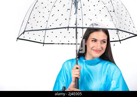 Scatto da studio di bella, felice e sorridente donna con lunghi capelli scuri indossando impermeabile blu e nascondendosi sotto trasparente con punti neri stile retrò Foto Stock