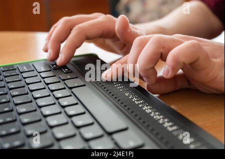 Un uomo cieco utilizza un computer con un display Braille e una tastiera per computer. Dispositivo incluso. Foto Stock