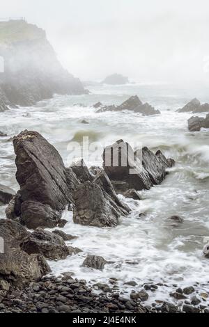 Quando la marea sale, uno strato di nebbia che si deforma nasconde la costa frastagliata di Hartland Point nel Devon settentrionale. Foto Stock