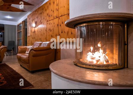 Caminetto in vetro accanto a un divano in pelle nella lobby di stile rustico nel lussuoso resort Foto Stock