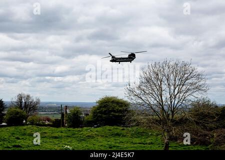 Un elicottero Royal Air Force CH-47 Chinook vola in basso e vicino oltre il mulino a vento a Brill, Buckinghamshire, Regno Unito, in una giornata di primavera con le nuvole grigie basse. Foto Stock