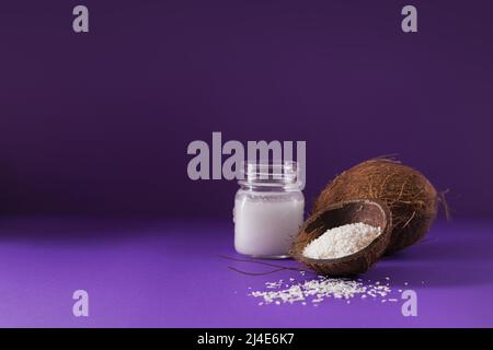 Cocco, fiocchi e olio di cocco in vaso su sfondo viola Foto Stock