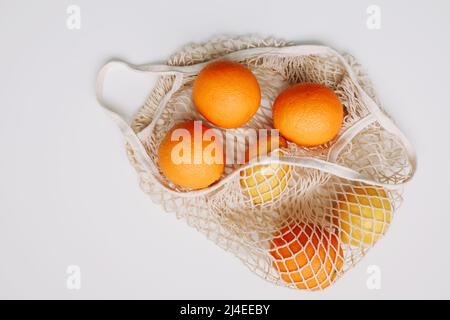 Limoni in sacchetto riutilizzabile. Concetto zero rifiuti con sacco a cordoncino, sacchetto in rete, sacchetto per grosery con frutta su sfondo bianco, piatto, vista dall'alto, spazio copia Foto Stock