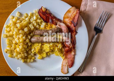 salsiccia e pancetta con uova strapazzate e un lato di crocchette di patate Foto Stock