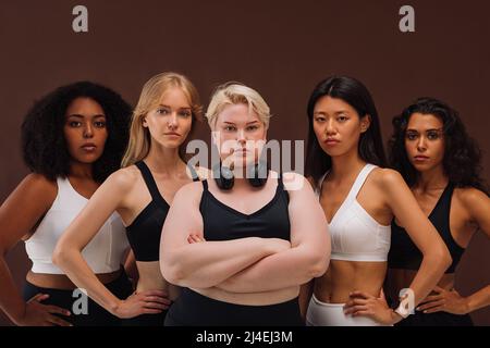 Cinque donne sicure in abbigliamento sportivo in piedi insieme. Femmine di diversi tipi di corpo che guardano la fotocamera. Foto Stock