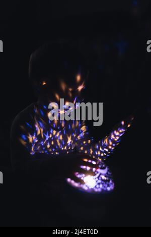 Scatto verticale. Foto scura. Ricordi notturni. Ragazzo che gioca con il proiettore di luce. Foto di alta qualità Foto Stock