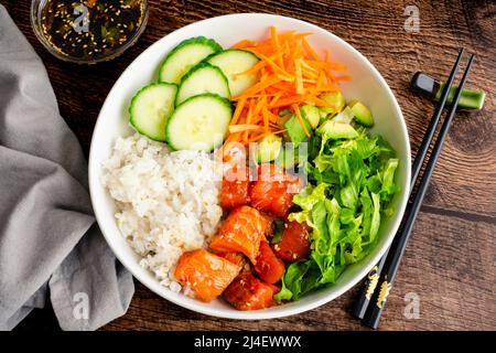 Spicy Salmon Sushi Bowl con verdure e riso: Ingredienti a base di sushi roll a base di salmone serviti in un recipiente poco profondo con salsa da immersione e bacchette Foto Stock