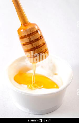 Il miele gocciola dal tuffatore in una tazza di yogurt fondo bianco isolato Foto Stock