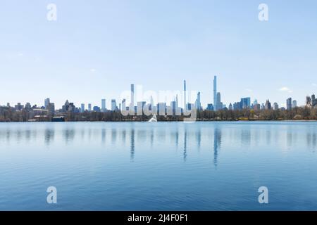 Panorama dello skyline della fila di miliardari visto attraverso il bacino idrico di Central Park con il geyser al centro con un cielo blu chiaro Foto Stock