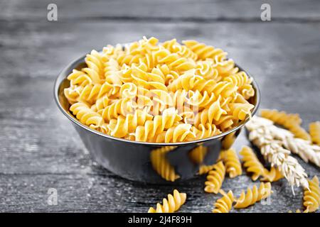 Farina integrale di grano fusilli in una ciotola, spikelets di grano su un fondo di legno scuro del bordo Foto Stock