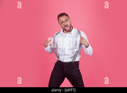 Uomo felice, stupito, soddisfatto e sorpreso. Ritratto di divertente funky pazzo uomo con sospendenti isolato su sfondo rosa. Foto Stock