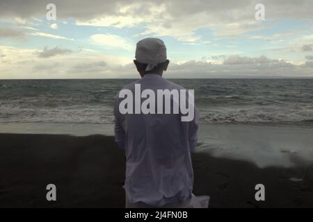 Purificare gli spiriti: Un prete che prega mentre guarda verso il mare durante un rituale della famiglia Balinese alla spiaggia di Goa Lawah in Klungkung regency, Bali, Indonesia. © Reynold Sumayku Foto Stock