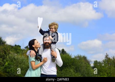 Famiglia felice padre madre e figlio bambino ridendo e havig divertimento con aereo di carta giocattolo. Bambino che gioca con l'aeroplano giocattolo e sognando futuro, concetto Foto Stock