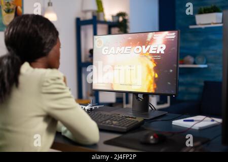 Sconvolto pro gamer donna che gioca spazio sparatutto videogiochi perdere campionato online. Giocatore nervoso afroamericano che usa l'apparecchiatura del calcolatore RGB seduta nello studio domestico di gioco. Torneo di eSport Foto Stock