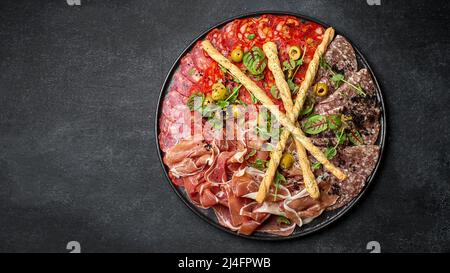 Affettato da diversi tipi di salsiccia e jamon, su un piatto, su sfondo scuro con un posto per il testo Foto Stock