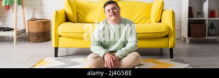 Adolescente felice con sindrome di Down seduta sul pavimento a casa, banner Foto Stock