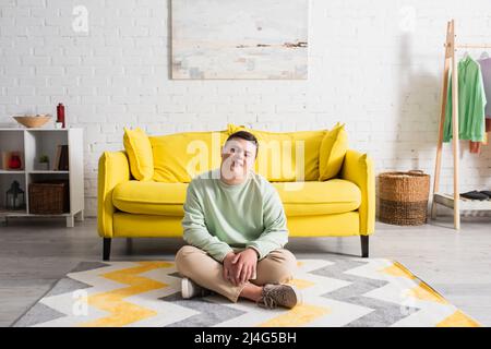 Adolescente positivo con sindrome di Down seduta sul pavimento a casa Foto Stock