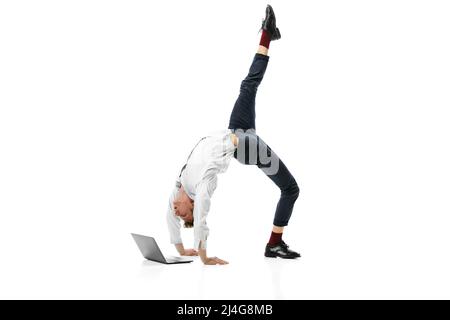 Ritratto creativo di giovane uomo flessibile che fa backbend e digitando su laptop isolato su sfondo bianco studio. Business nel concetto di vita moderna Foto Stock