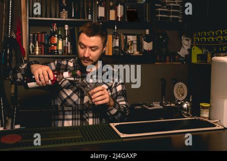 Barman preparare un cocktail dietro il bancone del bar, versando il liquore di bacche in un bicchiere Foto Stock