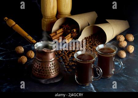 Turk e due tazze di caffè caldo con spezie, noci e chicchi di caffè su sfondo scuro. Oscuro e moody Foto Stock