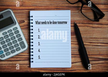 Per visualizzare il testo su blocco note - cosa si deve fare domani con calcolatrice, penna e occhiali su tavola di legno. Foto Stock