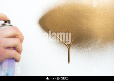 mano sfocata che tiene una latta di vernice di colore dorato, dipingendo una superficie bianca Foto Stock