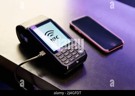 Terminale POS approvato per il pagamento, Payment Machine con telefono cellulare su sfondo scuro. Pagamento senza contatto con tecnologia NFC. Foto Stock