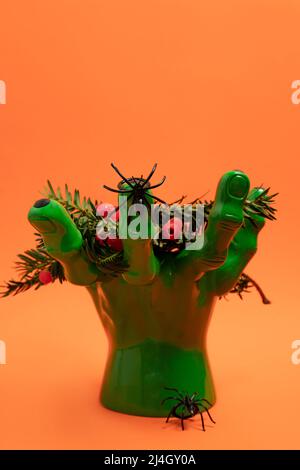 Mano verde che tiene rami di tasso con bacche rosse e due ragni. Concetto di decorazione di Halloween Foto Stock