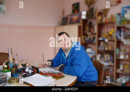 un uomo adulto con sindrome di down è impegnato a disegnare in un laboratorio. Foto Stock