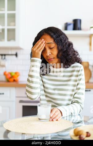 Donna afroamericana che si occupa di mal di testa. Sciogliendo la pillola in un bicchiere d'acqua Foto Stock