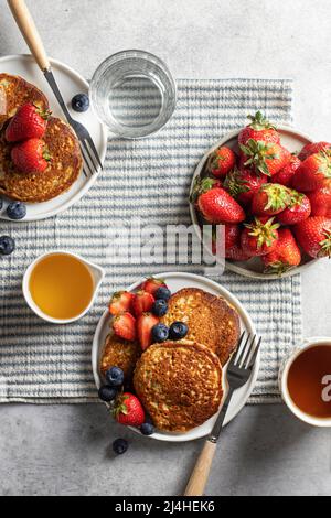 Colazione a base di pancake con frutti di bosco e miele per due su una tovaglia a righe. Vista dall'alto. Orientamento verticale Foto Stock