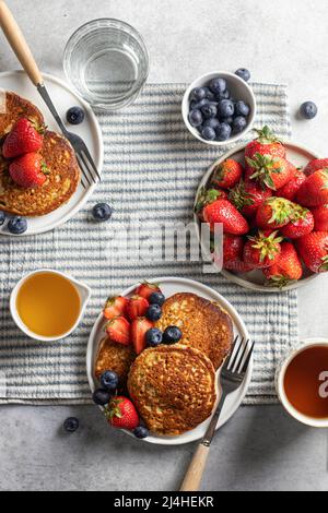 Colazione a base di pancake con fragole e mirtilli e miele per due su una tovaglia a righe con tè. Vista dall'alto Foto Stock