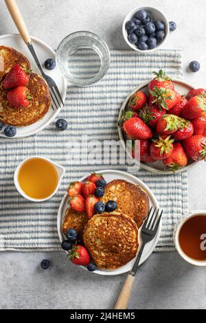 Colazione a base di pancake con fragole e mirtilli e miele per due su una tovaglia a righe. Vista dall'alto Foto Stock