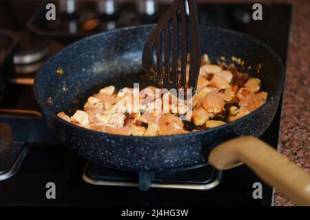 Donna mescolando pezzi di carne e friggere in padella in stufa Foto Stock