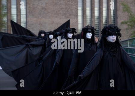 Londra, Regno Unito. 15th Apr 2022. Gli attivisti si esibiscono mentre camminano lungo il Millennium Bridge. Gli attivisti del gruppo di proteste sul clima Extinction Rebellion vestito da brigate nere e si esibiscono in mimi, movimenti al rallentatore e tableaux in pubblico per protestare contro gli investimenti di combustibili fossili da parte del governo britannico e l'impatto dei combustibili fossili per l'ambiente. Credit: SOPA Images Limited/Alamy Live News Foto Stock