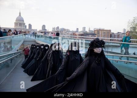 Londra, Regno Unito. 15th Apr 2022. Gli attivisti si esibiscono mentre camminano lungo il Millennium Bridge. Gli attivisti del gruppo di proteste sul clima Extinction Rebellion vestito da brigate nere e si esibiscono in mimi, movimenti al rallentatore e tableaux in pubblico per protestare contro gli investimenti di combustibili fossili da parte del governo britannico e l'impatto dei combustibili fossili per l'ambiente. (Foto di Hesther ng/SOPA Images/Sipa USA) Credit: Sipa USA/Alamy Live News Foto Stock