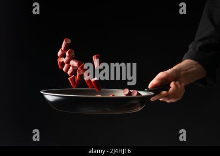 Lo chef sta cucinando salsicce di peperoni, su sfondo nero, un libro di ricette, salsicce tedesche, spuntini alla birra Foto Stock