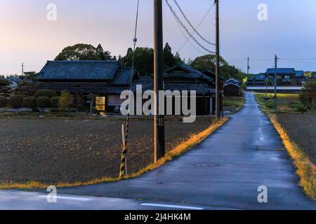 Strada bagnata attraverso la campagna giapponese che conduce alle case tradizionali al tramonto Foto Stock