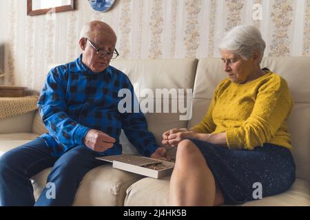 Coppia europea senior che assemblano puzzle in legno insieme. Attività per il tempo libero. Pensionamento attivo. Foto di alta qualità Foto Stock