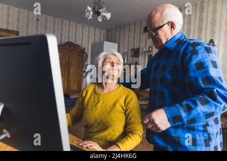 La coppia caucasica del pensionato che fa lo shopping in linea e paga le loro fatture in linea via il calcolatore. Moderno concetto di anziani. Foto di alta qualità Foto Stock