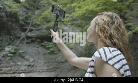 Donna prende belle viste di montagna al telefono con stabilizzatore. Azione. Scatti professionali al telefono grazie al cavalletto palmare stabilizzante. Manuale Foto Stock
