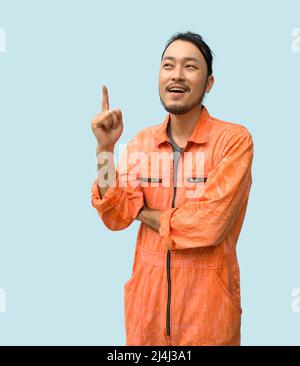 Il meccanico principale in una uniforme arancione che punta un dito verso l'alto. Ritratto su sfondo blu con luce da studio. Foto Stock