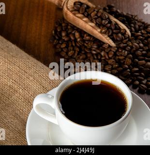 Tazza bianca di caffè con chicchi di caffè su sfondo di legno Foto Stock