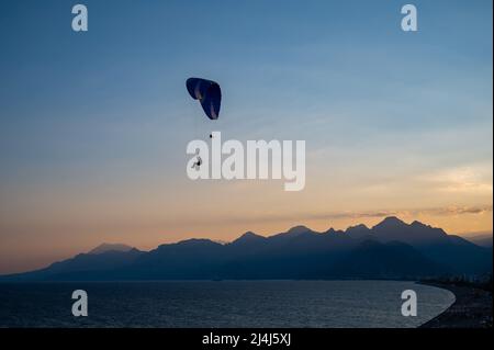 Silhouette di un uomo su un parapendio che vola sul mare al tramonto. Foto Stock