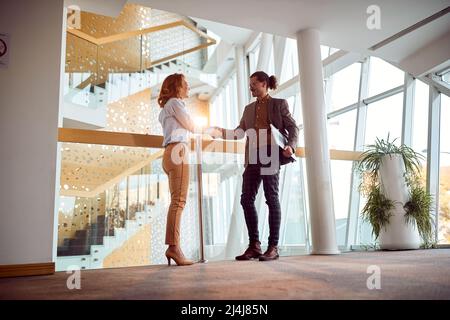Un giovane uomo d'affari si sta scuotendo a mano con una collega in un'atmosfera piacevole nel corridoio di costruzione dell'azienda. Aziende, persone, aziende Foto Stock