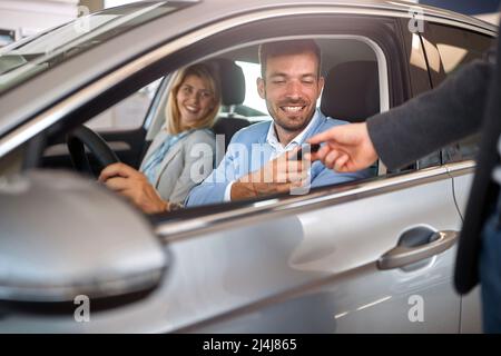 Acquirente con donna in auto nuova prendendo la chiave dal venditore Foto Stock