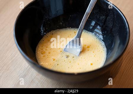 i tuorli d'uovo sbattuti e la glassa di latte in un recipiente nero per spalmare dolci come le trecce di pasqua Foto Stock