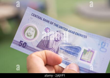 Persone che danno la valuta degli Emirati Arabi Uniti (Emirati Arabi Uniti) - nuovi 2021 cinquanta note Dirham sparse su sfondo verde. Cambio valuta. Foto Stock